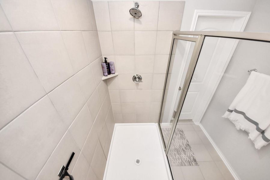 View of the large tiled walk in shower as taken hign above and looking down into the shower. Glass shower door entrance is on the right. White door leads to the toilet room. View of the large tiled walk in shower as taken hign above and looking down into the shower. Glass shower door entrance is on the right. White door leads to the toilet room.