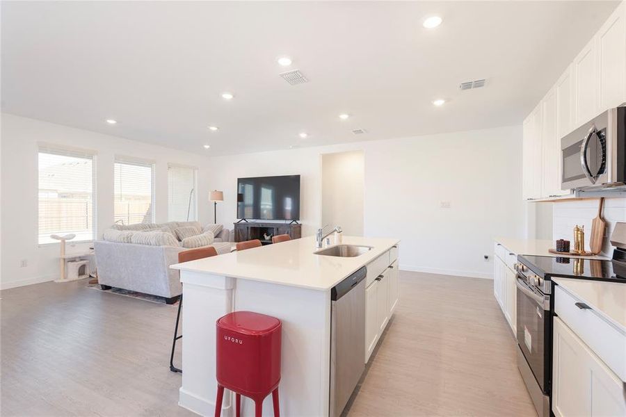 Kitchen with stainless steel appliances, white cabinets, open floor plan, recessed lighting, and a breakfast bar Kitchen with stainless steel appliances, white cabinets, open floor plan, recessed lighting, and a breakfast bar
