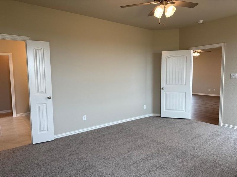 Carpeted room featuring a ceiling fan with light fixture, painted walls, white trim, and two paneled doors with brushed nickel hardware