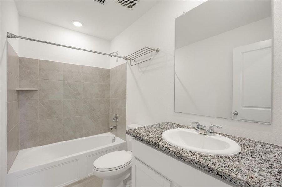 Bathroom featuring a white bathtub, tiled shower surround with built-in shelf, white vanity with speckled countertop, and a wall-mounted mirror