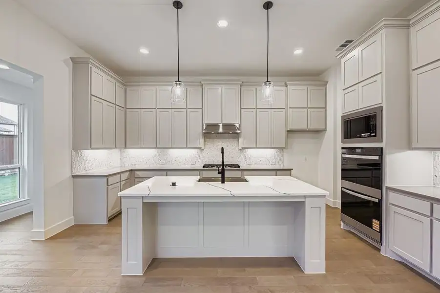 Kitchen with backsplash, light wood-type flooring, a kitchen bar, a center island with sink, and recessed lighting