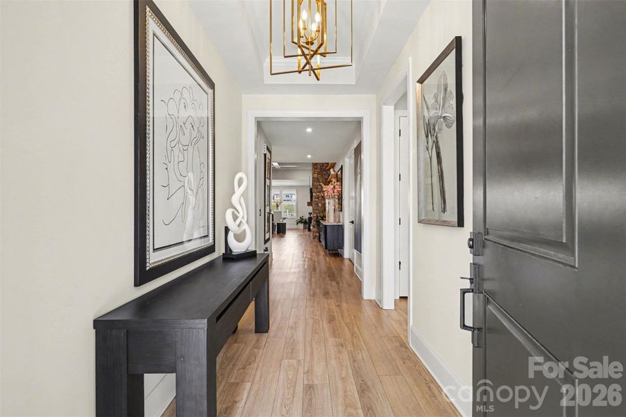 A bright, inviting modern foyer featuring light French oak EVP flooring, a bold gold geometric chandelier.