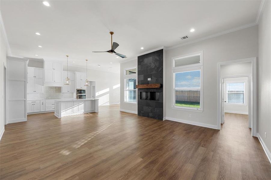 Unfurnished living room featuring dark wood-style flooring, a ceiling fan, ornamental molding, recessed lighting, and a tiled fireplace Unfurnished living room featuring dark wood-style flooring, a ceiling fan, ornamental molding, recessed lighting, and a tiled fireplace