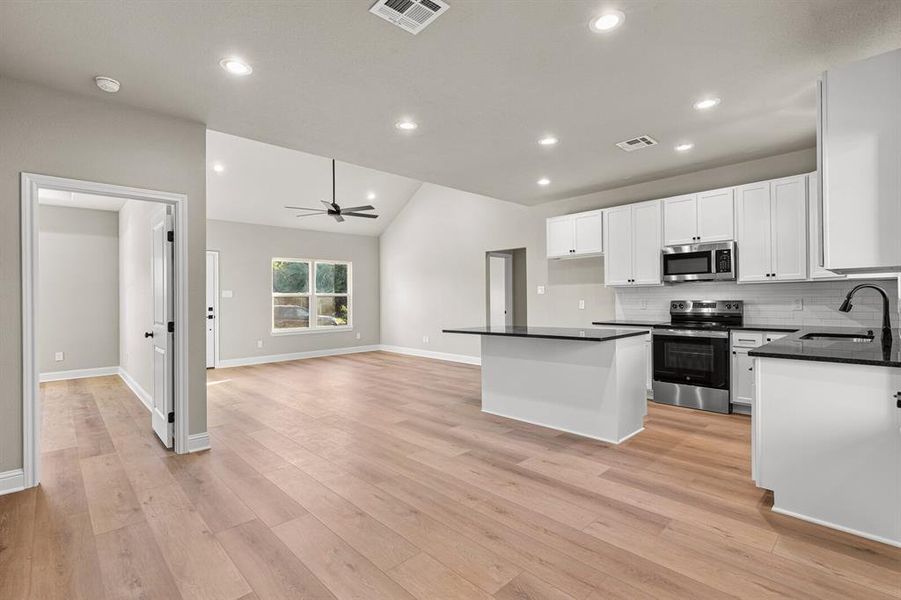 Kitchen featuring appliances with stainless steel finishes, white cabinetry, backsplash, a ceiling fan, and lofted ceiling Kitchen featuring appliances with stainless steel finishes, white cabinetry, backsplash, a ceiling fan, and lofted ceiling