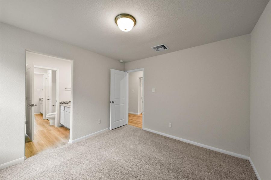 Cozy carpeted bedroom featuring neutral tones and a private en-suite with a granite-topped vanity.