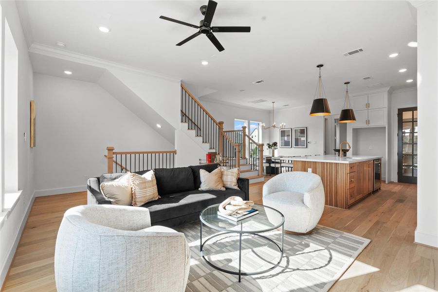 Spacious, open-concept living area is well-lit with natural light and has a cozy seating area with stylish decor and a contemporary staircase leading to the upper floor.