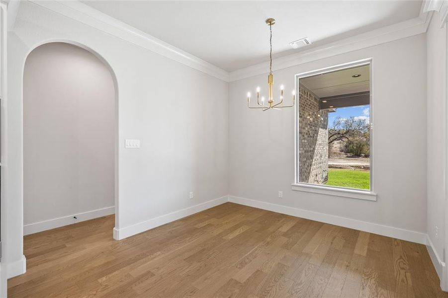 Unfurnished dining area featuring arched walkways, crown molding, a chandelier, and light wood-style floors