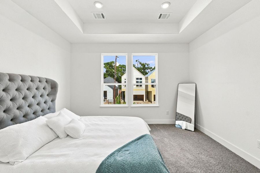 Spacious primary bedroom featuring a tray ceiling with recessed lighting, large windows providing abundant natural light, and plenty of room for additional furniture. Spacious primary bedroom featuring a tray ceiling with recessed lighting, large windows providing abundant natural light, and plenty of room for additional furniture.