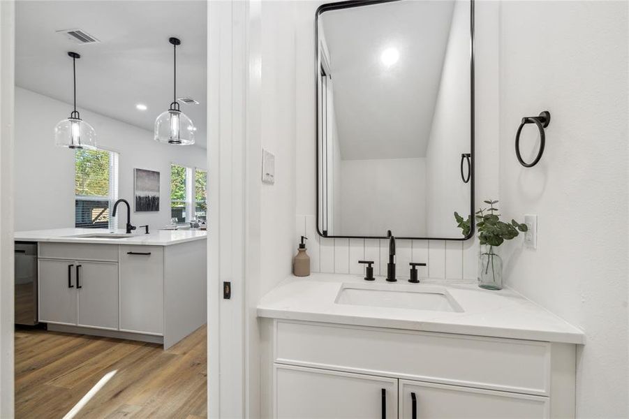 Chic half bath off the kitchen featuring a sleek black-framed mirror, modern fixtures, and a minimalist design that complements the open-concept living space visible just beyond.