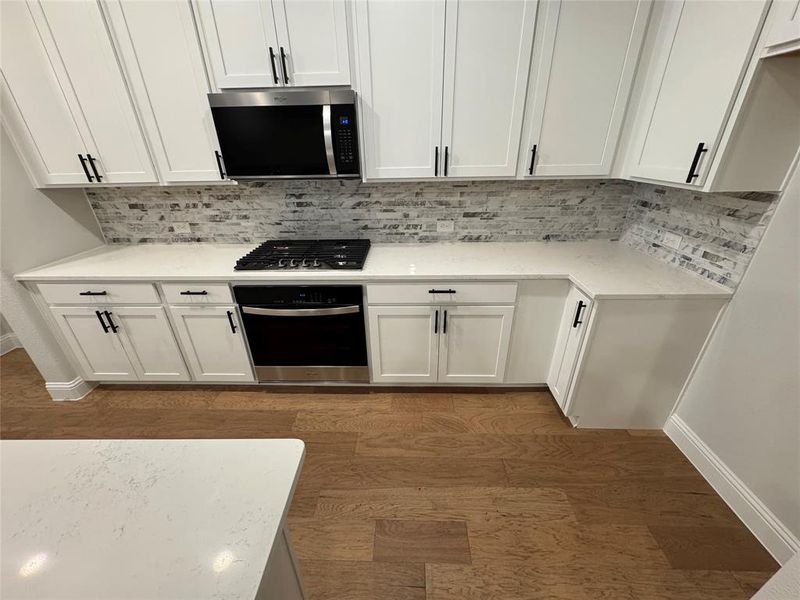 Modern kitchen featuring white cabinetry, light-toned countertops, a gas range with an oven, and a built-in microwave