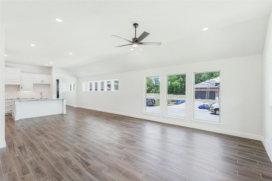 Open living area with dark hardwood floors, ceiling fan, and white kitchen visible in background Open living area with dark hardwood floors, ceiling fan, and white kitchen visible in background
