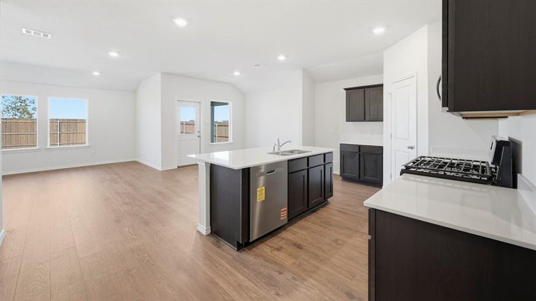 Kitchen with gas range, a center island with sink, light stone counters, dishwasher, and recessed lighting