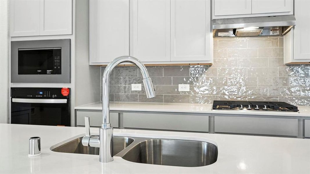 Kitchen featuring a dual basin sink with a gooseneck faucet, white shaker cabinetry, light-toned countertops, a built-in microwave, and a gas cooktop with a stainless steel range hood