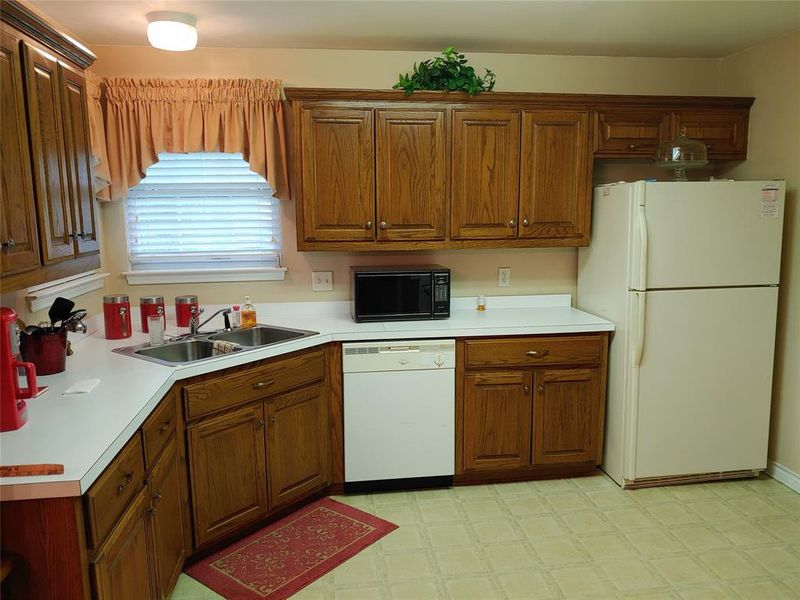 Kitchen featuring wood-finish cabinetry, white countertops, a double basin stainless steel sink, and patterned vinyl flooring
