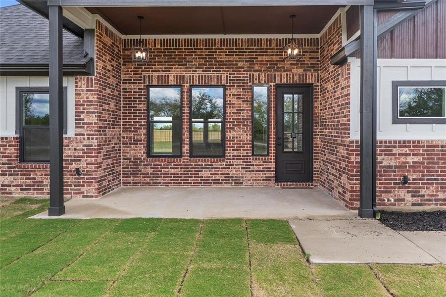 View of exterior entry featuring brick siding, a patio, and a lawn