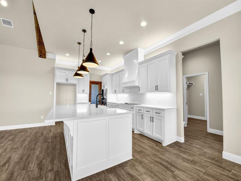 Kitchen with white cabinets, a center island with sink, and premium range hood