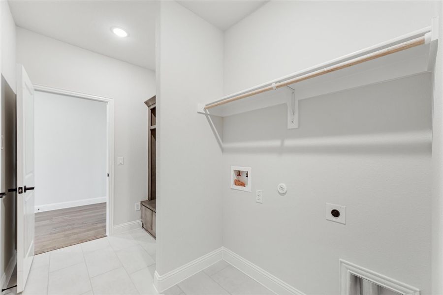 Laundry room with wall-mounted shelf, washer and dryer hookups, and tile floors leading to mudroom area.