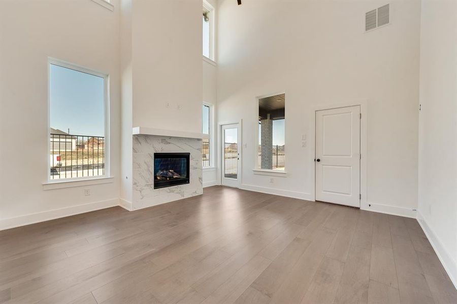 Unfurnished living room with a high end fireplace, light wood-type flooring, and a high ceiling Unfurnished living room with a high end fireplace, light wood-type flooring, and a high ceiling