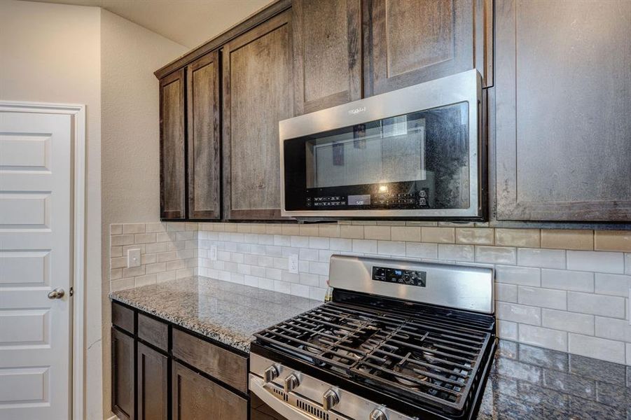 Kitchen with appliances with stainless steel finishes, backsplash, light stone countertops, and dark brown cabinetry Kitchen with appliances with stainless steel finishes, backsplash, light stone countertops, and dark brown cabinetry