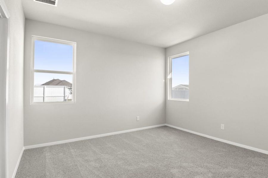 Image of a primary bedroom with tan carpeting, light grey walls, two windows and white trim