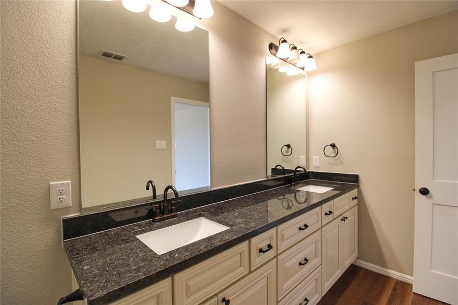 Bathroom with double vanity, a textured wall, and dark wood-style floors
