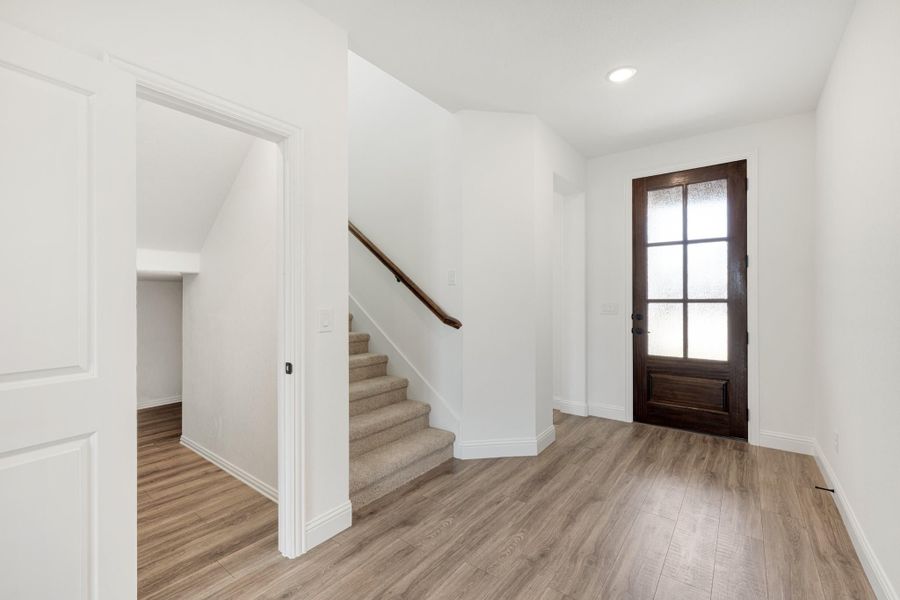 Entryway with wood-look floors, dark wood glass-panel front door, and carpeted staircase with wood railing Entryway with wood-look floors, dark wood glass-panel front door, and carpeted staircase with wood railing