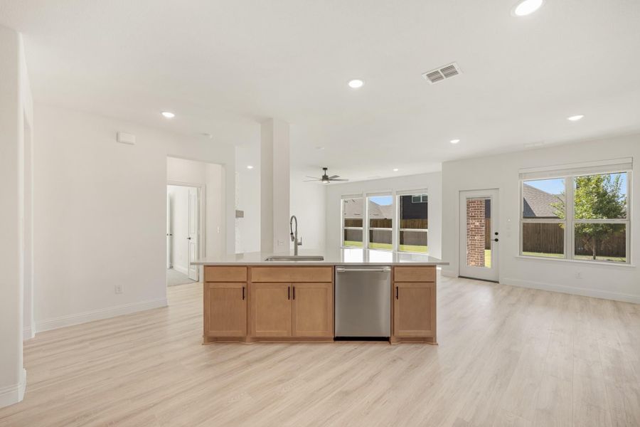Open-concept kitchen with wood cabinet island, stainless dishwasher, and light hardwood floors leading to living area