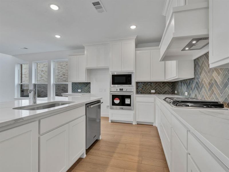 Kitchen with white cabinetry, light wood-type flooring, premium range hood, appliances with stainless steel finishes, and decorative backsplash