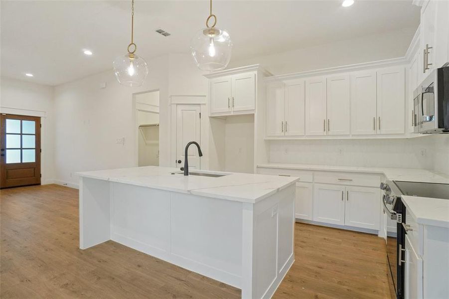 Kitchen with light stone counters, recessed lighting, light wood-type flooring, stainless steel microwave, and pendant lighting