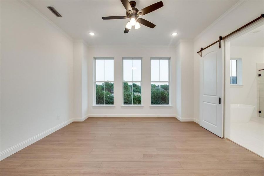 Unfurnished bedroom featuring ornamental molding, a barn door, light wood finished floors, a ceiling fan, and recessed lighting