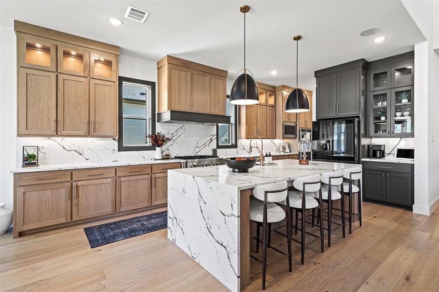 Kitchen featuring glass insert cabinets, a breakfast bar, an island with sink, tasteful backsplash, and recessed lighting Kitchen featuring glass insert cabinets, a breakfast bar, an island with sink, tasteful backsplash, and recessed lighting