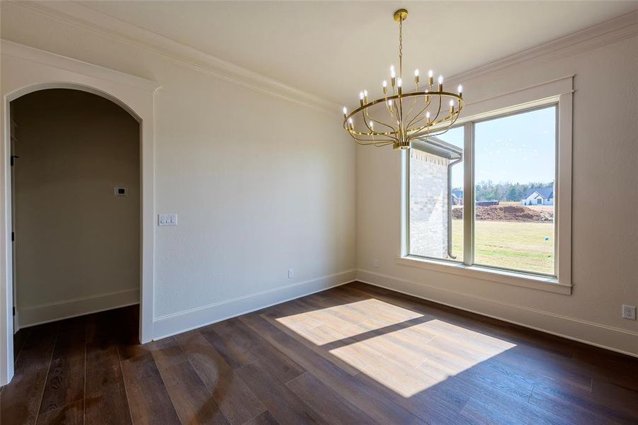 Spare room featuring crown molding, arched walkways, dark wood-style flooring, and suspended lighting