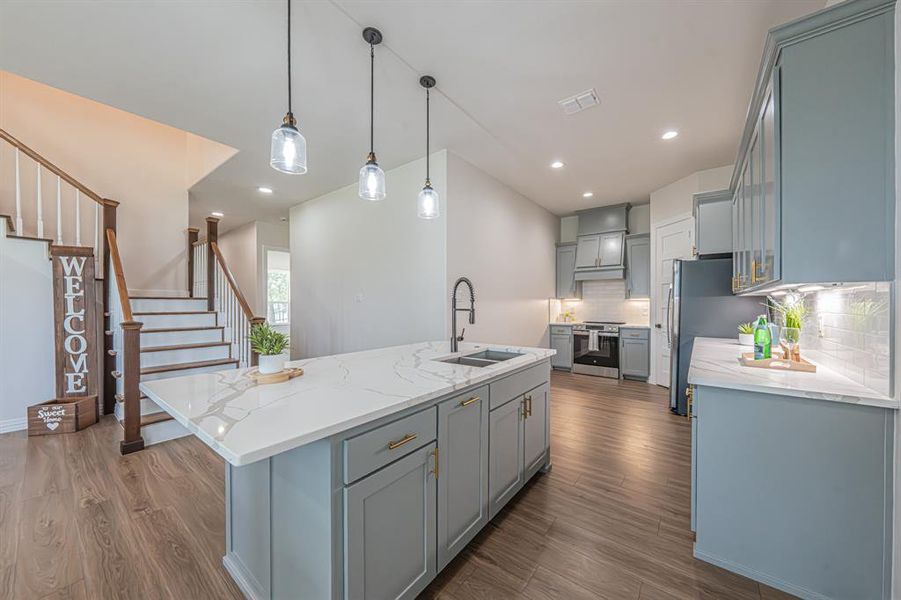 Kitchen with light stone counters, pendant lighting, an island with sink, gray cabinetry, and recessed lighting Kitchen with light stone counters, pendant lighting, an island with sink, gray cabinetry, and recessed lighting