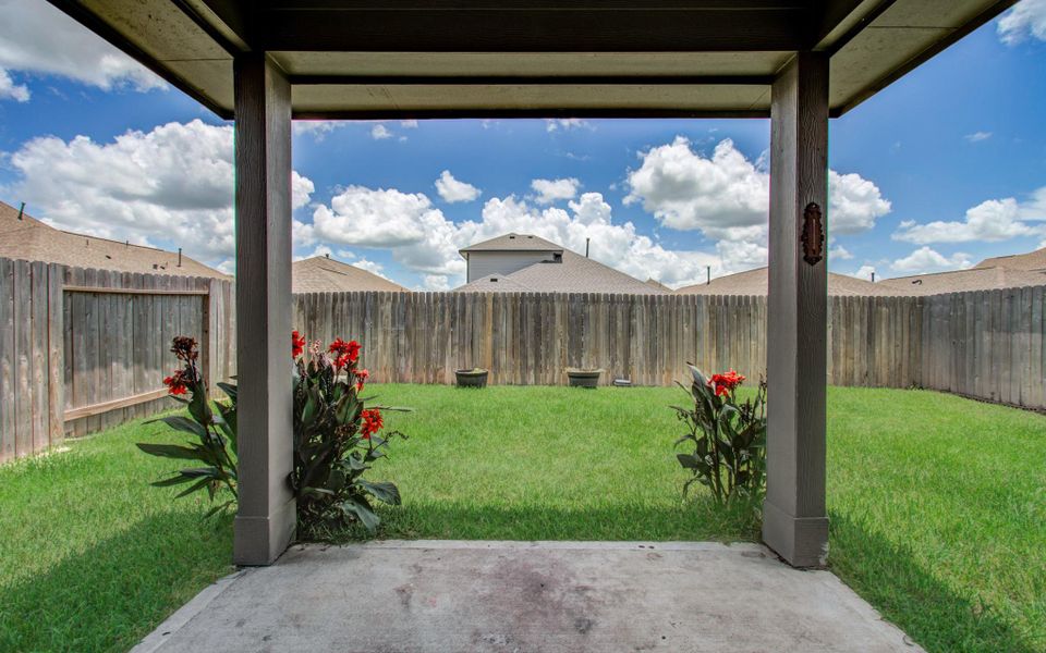 This photo features a fenced backyard with a small, covered patio. The lawn is well-maintained, and there are flowering plants on either side, providing a cozy outdoor space. This photo features a fenced backyard with a small, covered patio. The lawn is well-maintained, and there are flowering plants on either side, providing a cozy outdoor space.