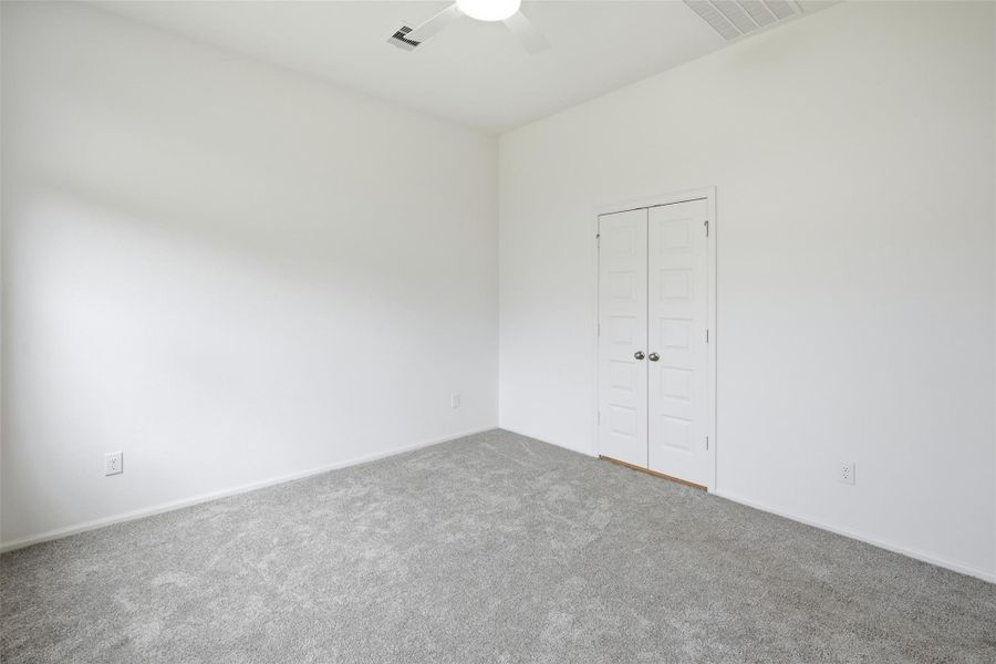 Bright and spacious room with soft carpeting, featuring a ceiling fan and a double-door closet for ample storage.