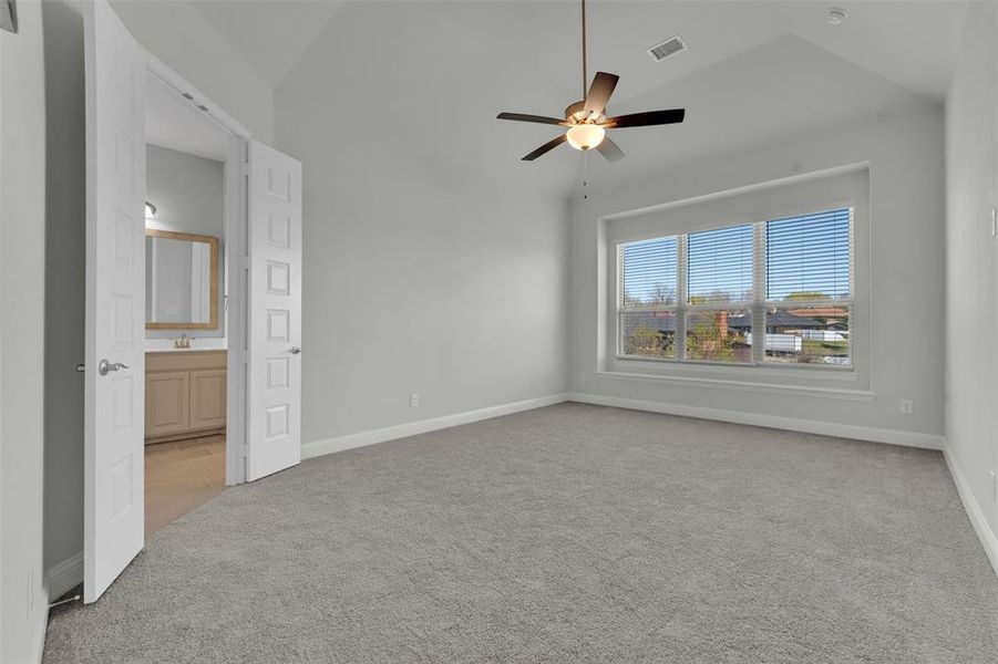 Unfurnished bedroom featuring light carpet, vaulted ceiling, a ceiling fan, and ensuite bath