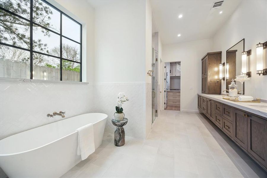 The spa-like primary bath includes a free-standing soaking tub, glass-enclosed shower, and a double vanity with rich wood cabinetry, offering a luxurious experience.