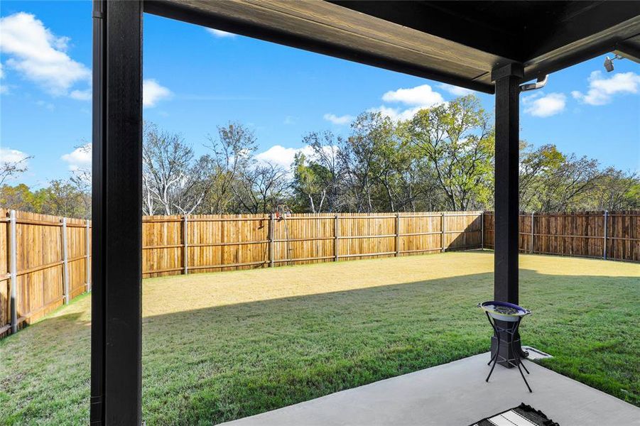 Covered patio extending to a spacious grass yard, featuring a complete wood privacy fence and mature perimeter trees