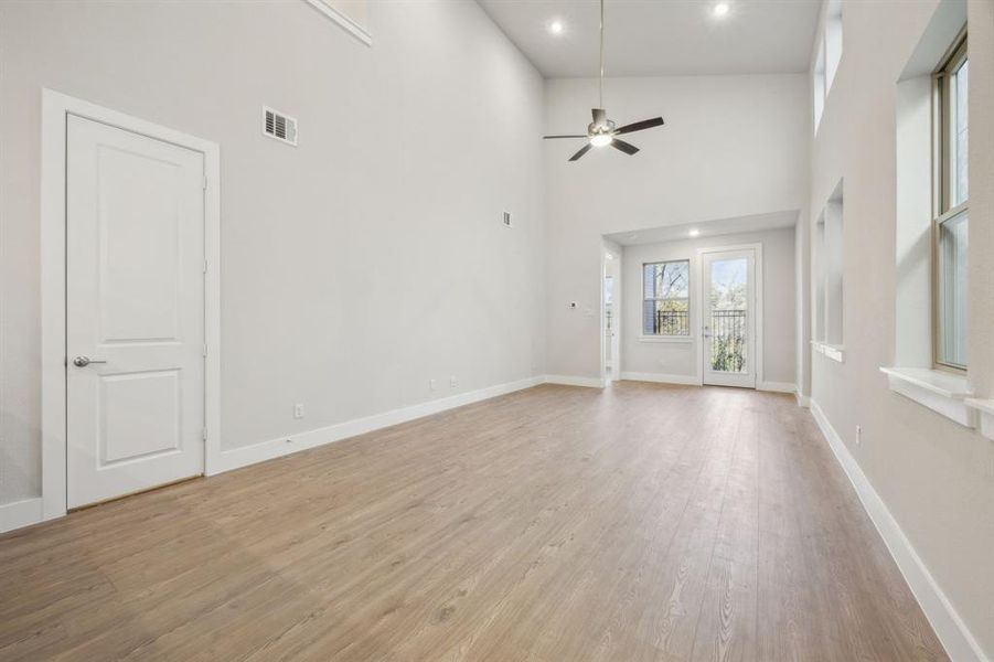 Unfurnished living room with light hardwood / wood-style floors, ceiling fan, and a high ceiling