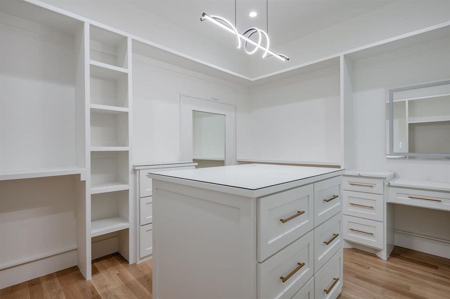 Walk in closet with light wood finished floors, a chandelier, and built in study area Walk in closet with light wood finished floors, a chandelier, and built in study area