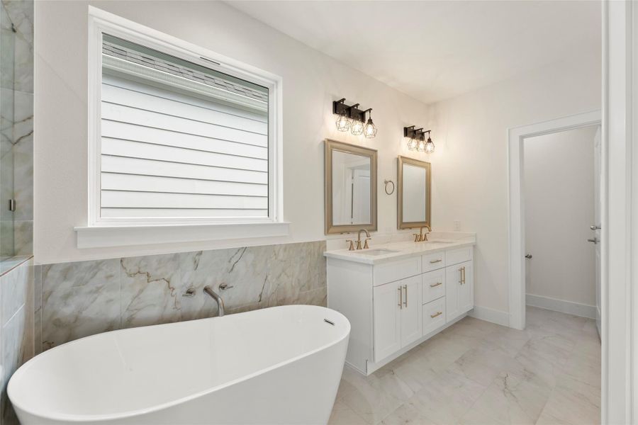 This modern bathroom features a freestanding tub, dual sinks with elegant fixtures, and ample natural light from a large window. The space is finished with sleek accents and contemporary lighting.