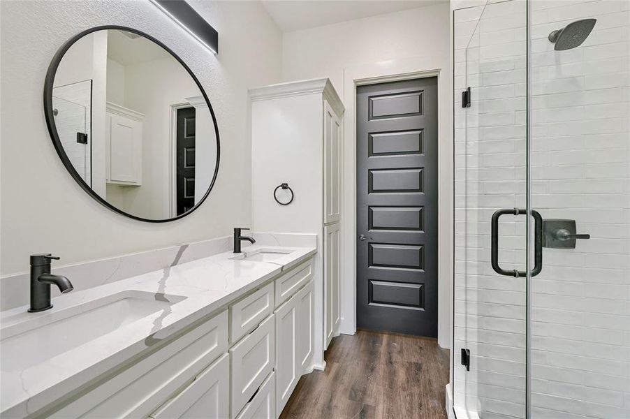 Full bathroom with wood finished floors, a sink, a stall shower, and double vanity