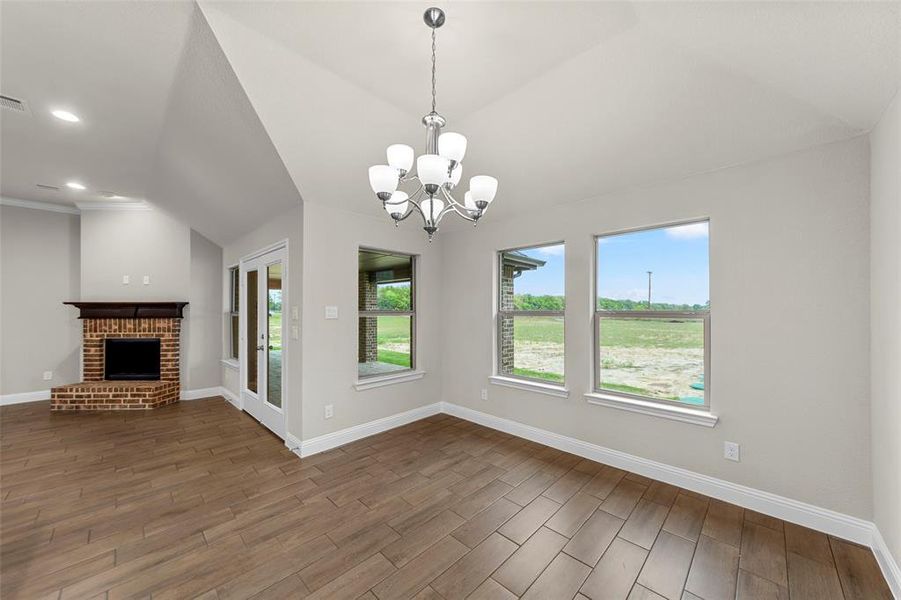 Open concept living space featuring vaulted ceilings, wood-finish flooring, a brick-surround fireplace with a wood mantle, and a glass-paneled door