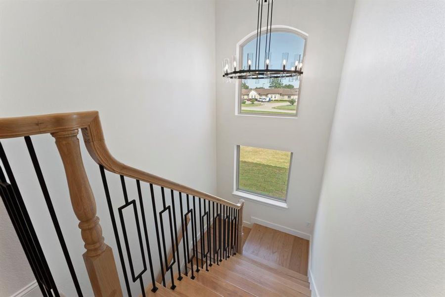 Elegant secondary stairwell with modern metal balusters, wooden handrail, and abundant natural light streaming through large windows, creating a bright and welcoming space.