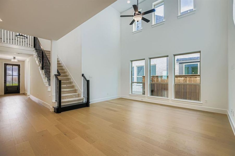 Unfurnished living room with stairway, light wood-type flooring, a high ceiling, and ceiling fan Unfurnished living room with stairway, light wood-type flooring, a high ceiling, and ceiling fan