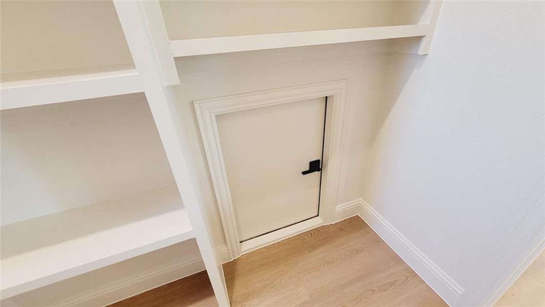 Built-in shelving unit featuring multiple open shelves, a small access door with black hardware, light wood-finish flooring, and white baseboards