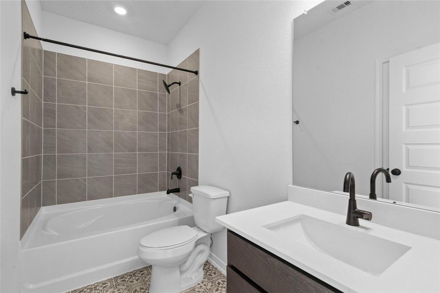 This move-in ready primary bathroom offers a spacious tub/shower combination with a tiled surround, stained cabinetry topped with light countertops, high ceilings, neutral paint, a mirror, and sleek, modern finishes for a polished look.