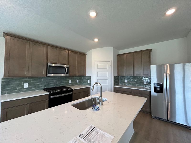Kitchen with stainless steel appliances, dark brown cabinets, light stone countertops, dark wood-type flooring, and tasteful backsplash Kitchen with stainless steel appliances, dark brown cabinets, light stone countertops, dark wood-type flooring, and tasteful backsplash