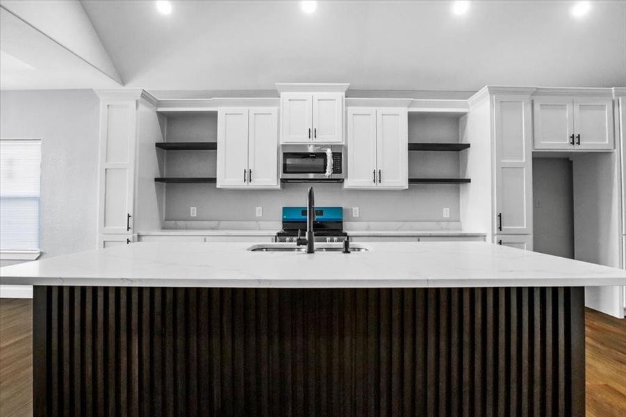 Kitchen featuring vaulted ceiling, light stone counters, an island with sink, dark hardwood / wood-style flooring, and white cabinetry