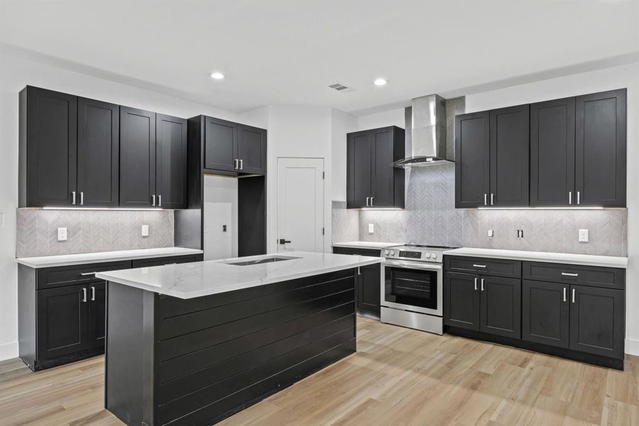 Kitchen featuring dark cabinets, light stone counters, tasteful backsplash, stainless steel electric stove, and light wood-type flooring